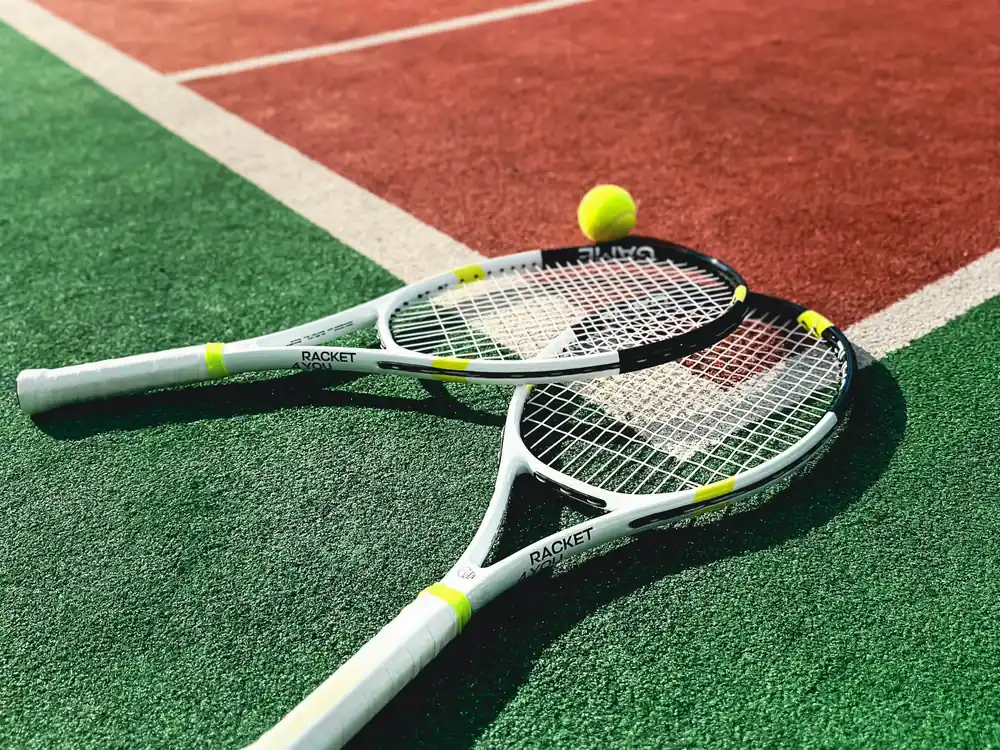 Two tennis rackets and a ball lying on a green and red tennis court