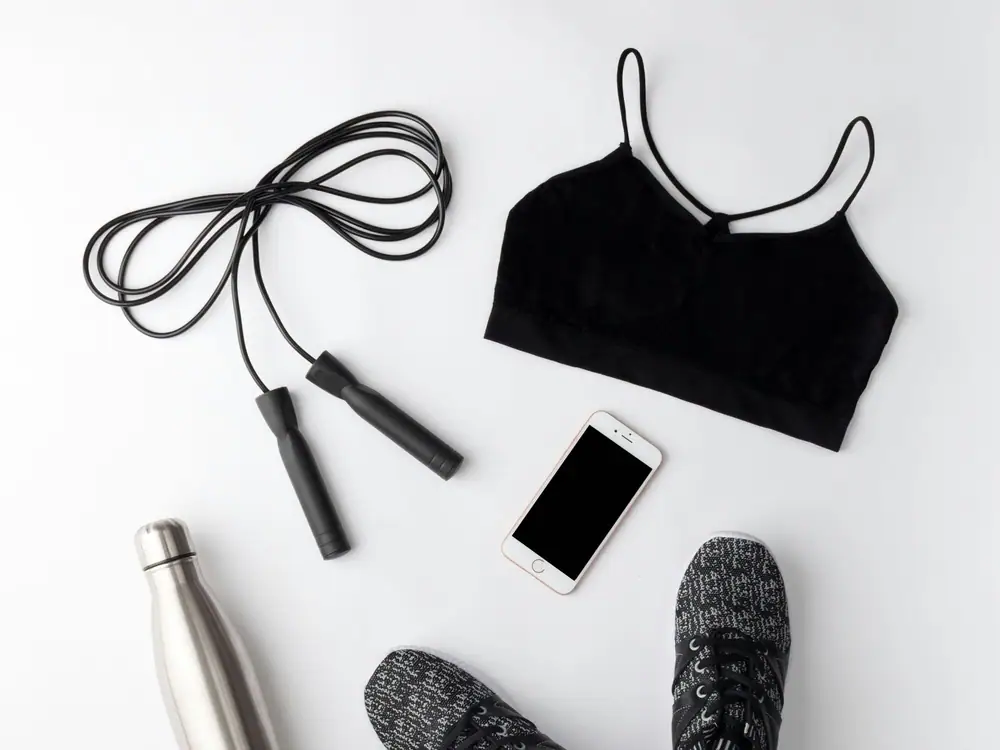Flat lay of a skipping rope, sports top, water bottle, phone and trainers on a white surface