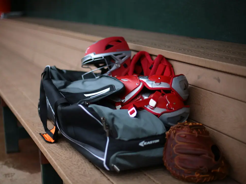 A sports bag with a helmet and glove on a wooden bench in a dugout