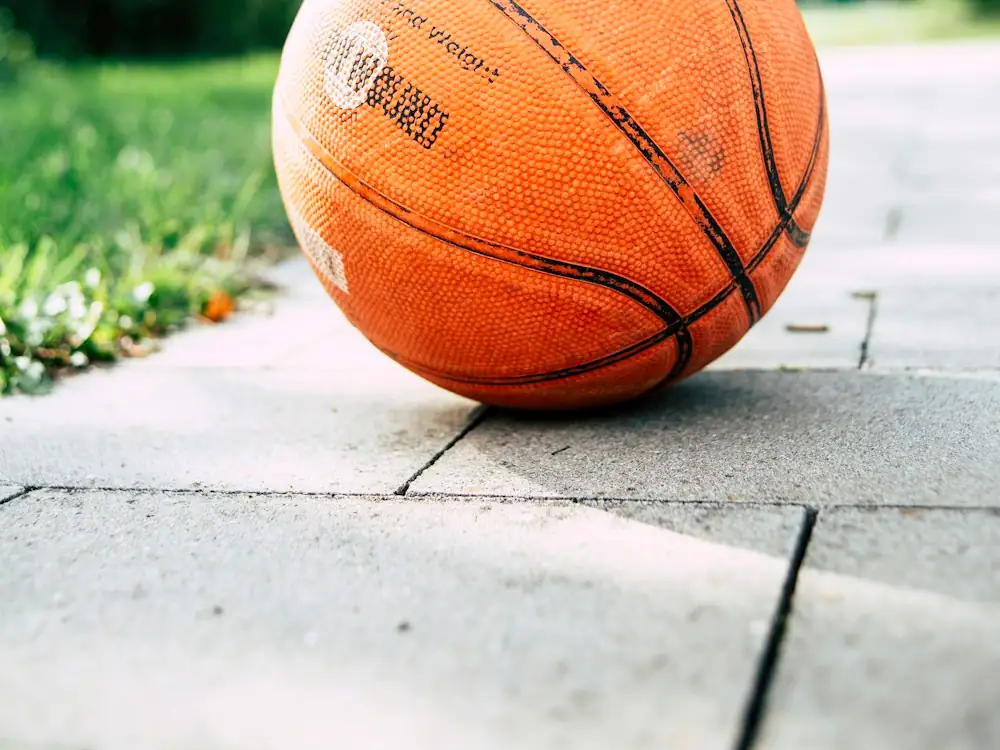 A well-used orange basketball resting on a path beside grass