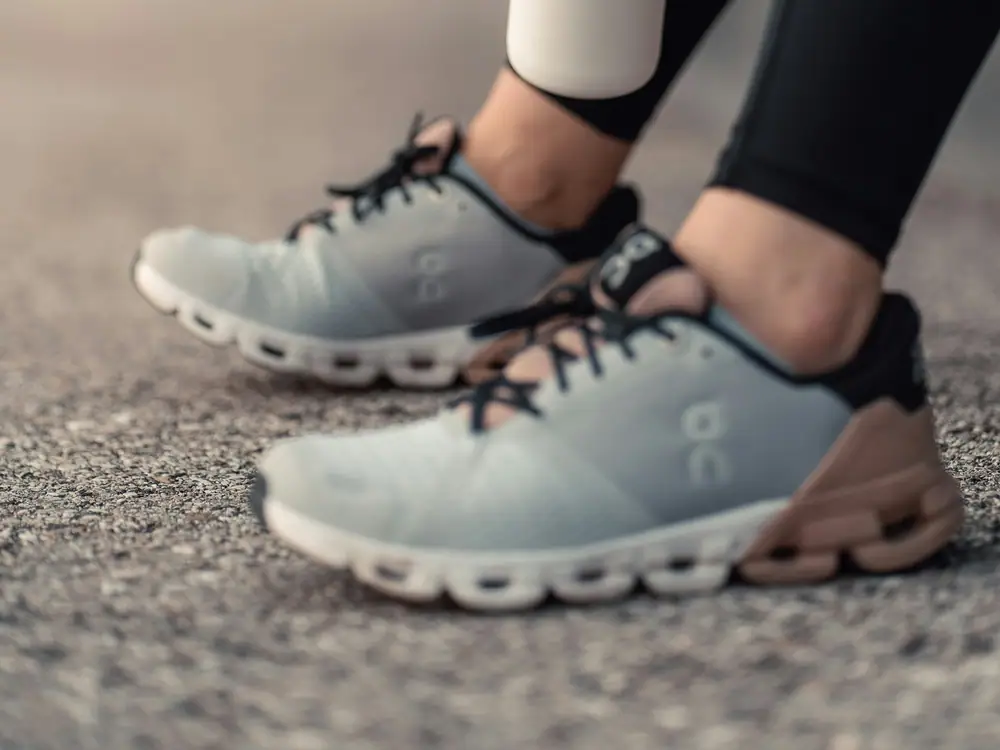 Close-up of a runner's feet in grey trainers standing on a path, holding a water bottle