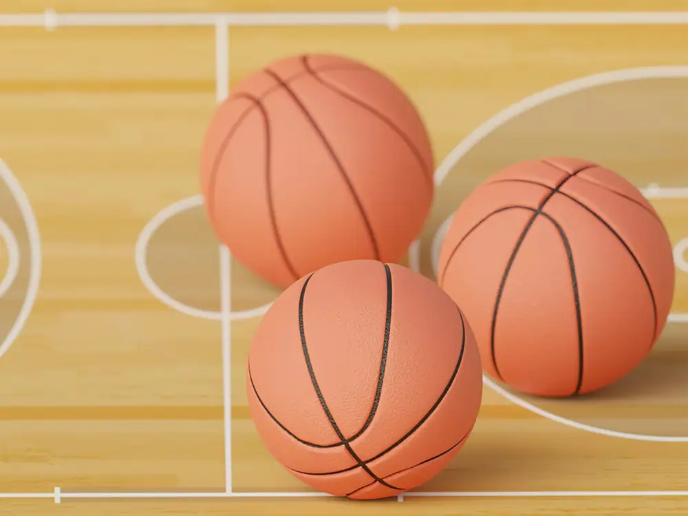 Three basketballs sitting on a wooden indoor basketball court