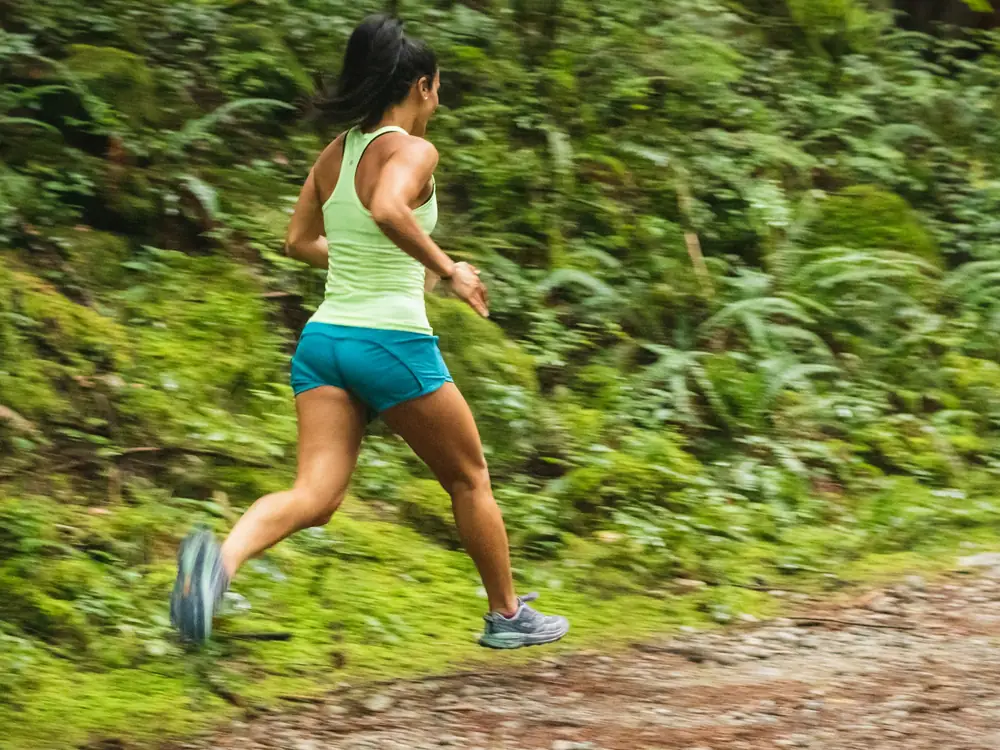 A woman running along a dirt path beside green bushes