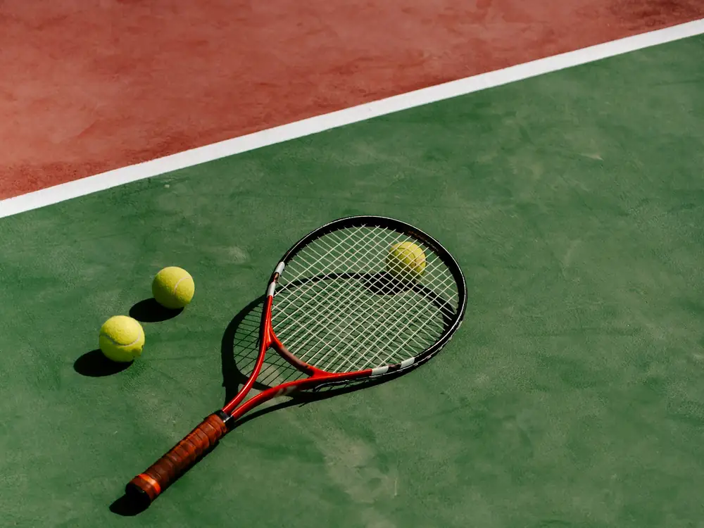 A tennis racket and three yellow tennis balls resting on a green hard court